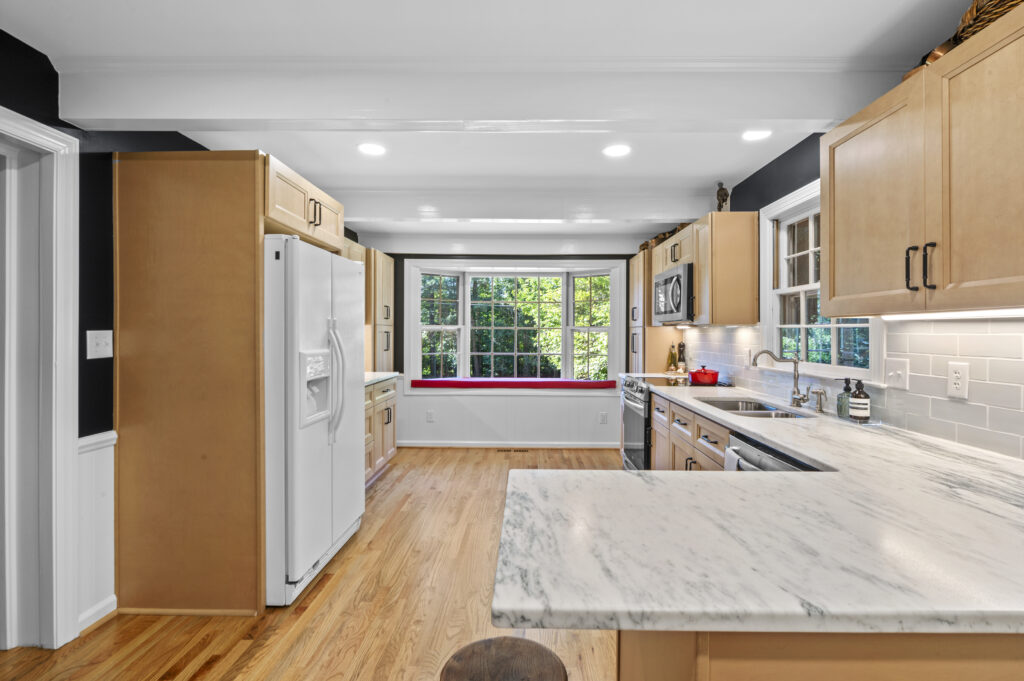 A remodeled kitchen showing appliances, countertops, and cabinets with a bay window at the end of the room